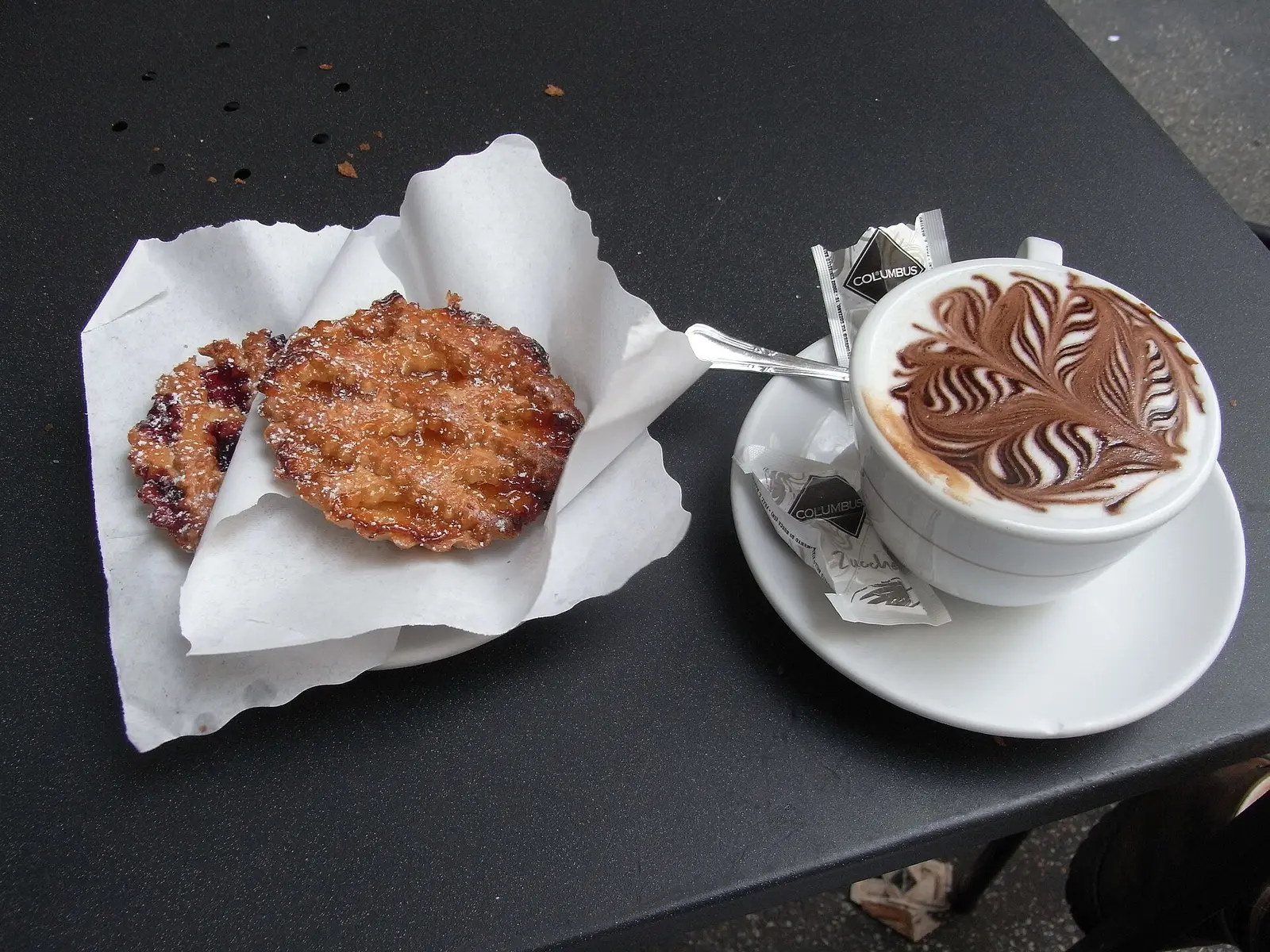A cappuccino with chocolate latte art beside two pastries on a cafe table.