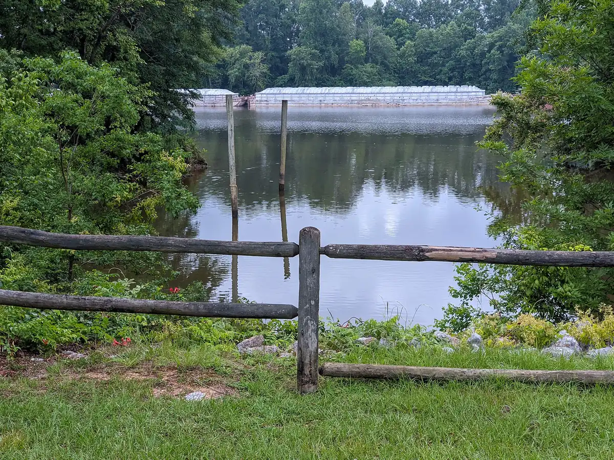 A split-rail fence on the bank of the Black Warrior River in Tuscaloosa, with barges moored across the water.