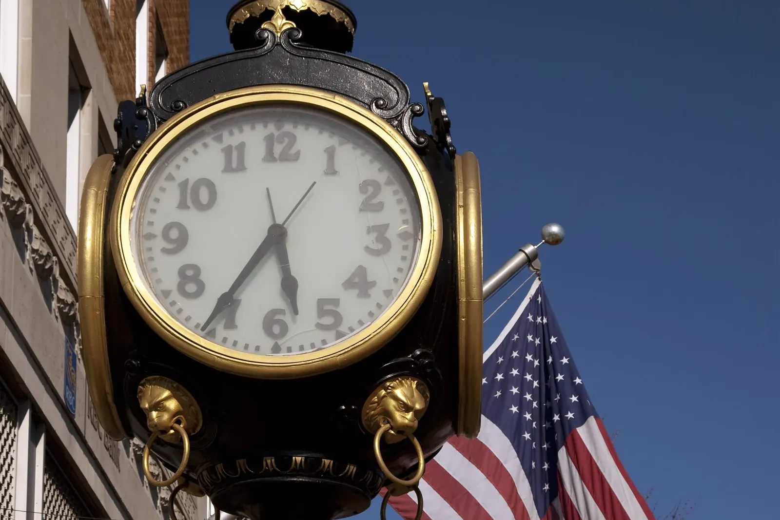A historic street clock and American flag on a downtown Tuscaloosa sidewalk.