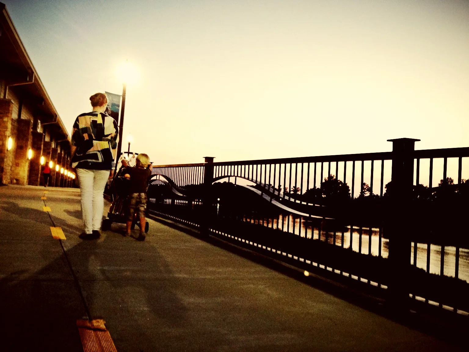 A mother and her children walk the Tuscaloosa Riverwalk along the Black Warrior River at sunset.