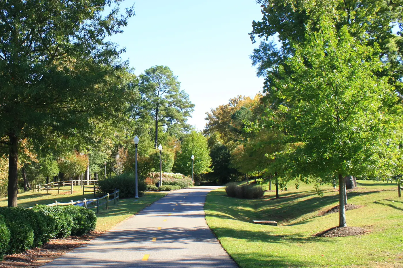 A paved stretch of the Riverwalk winds past lawns and lampposts along the Black Warrior River in Tuscaloosa.
