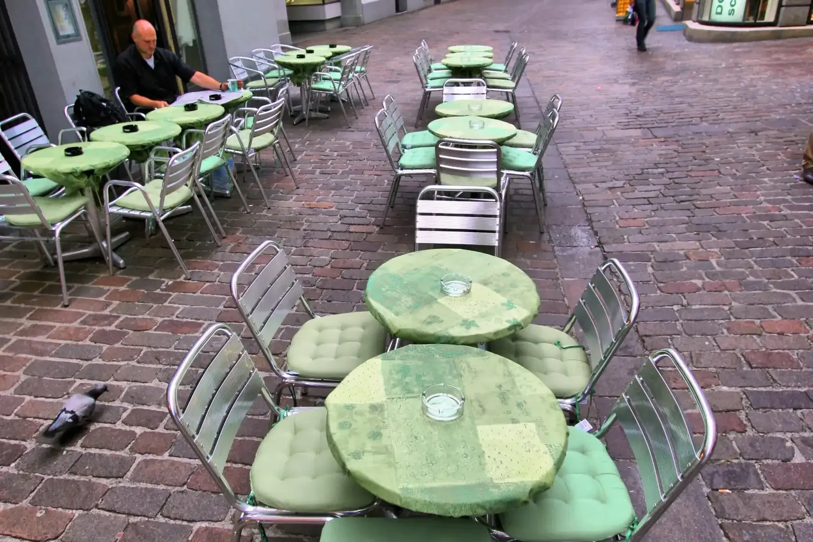 Cafe tables and cushioned chairs set out on a cobbled pedestrian street in St. Gallen, Switzerland.