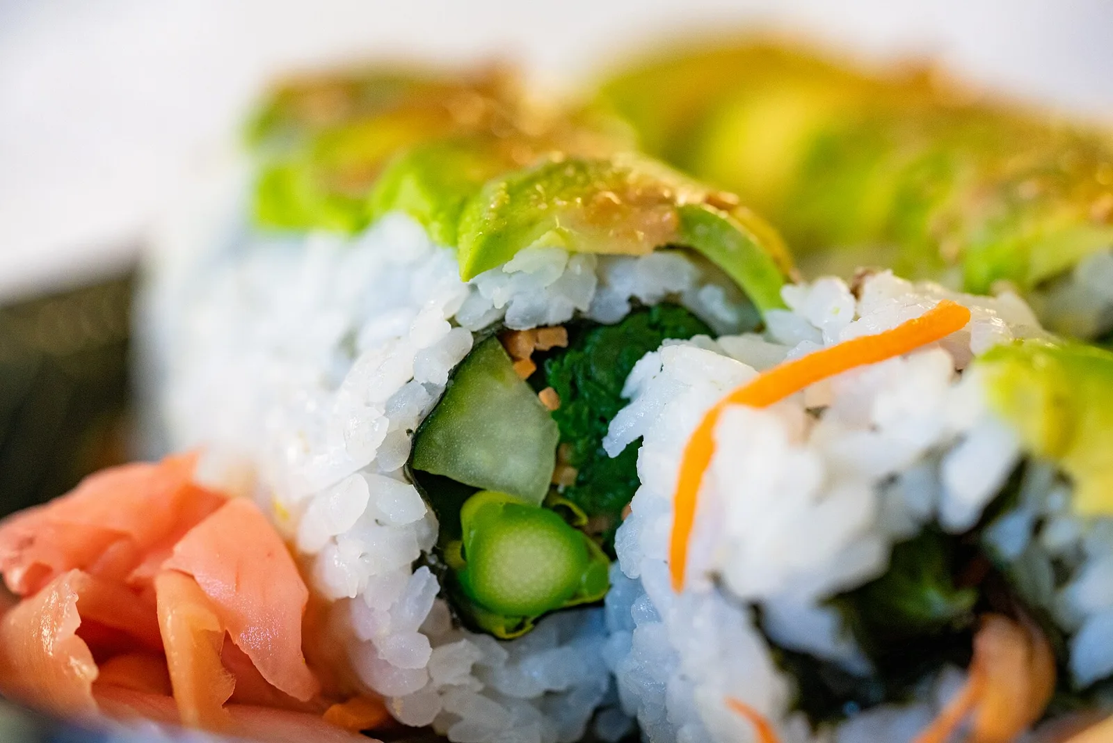 A close view of avocado-topped sushi rolls with asparagus and cucumber, beside pickled ginger.