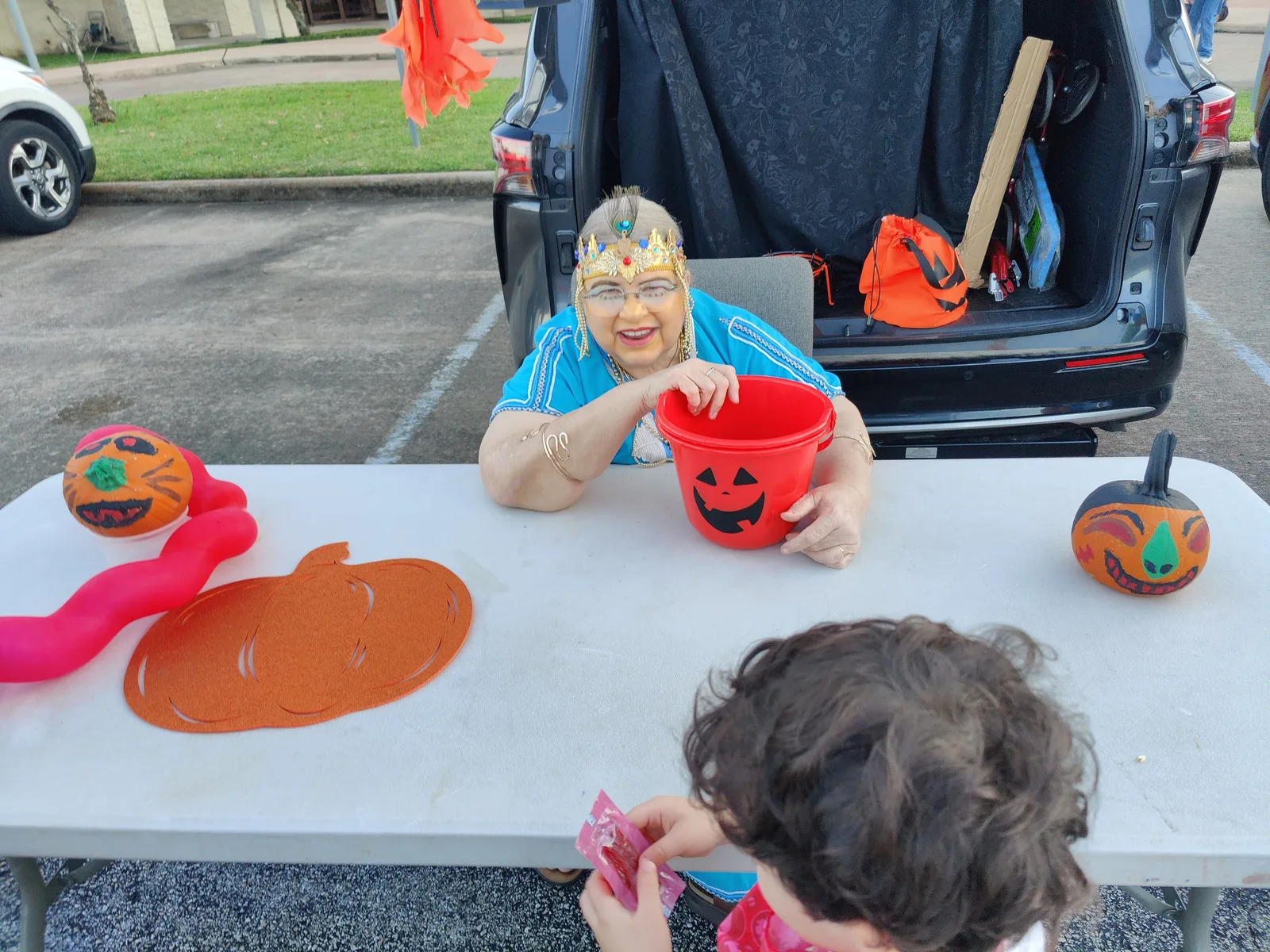 A volunteer in costume hands out candy from a decorated car trunk at a church trunk-or-treat event.