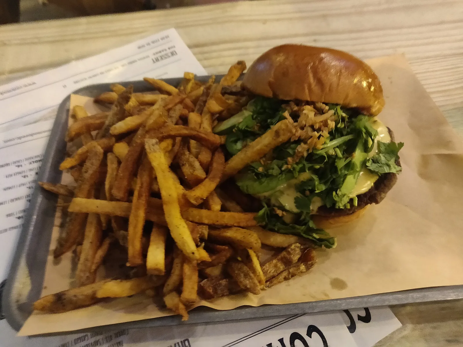 A cheeseburger topped with herbs and fried onions, served with fries on a metal tray.