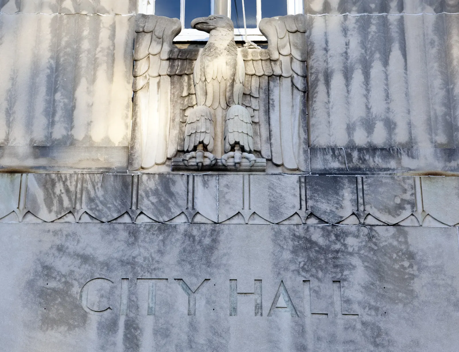 A carved stone eagle sits above the words "City Hall" on a downtown Tuscaloosa building.